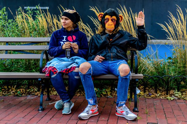 A photo of two people on a bench, including a guy in a monkey mask